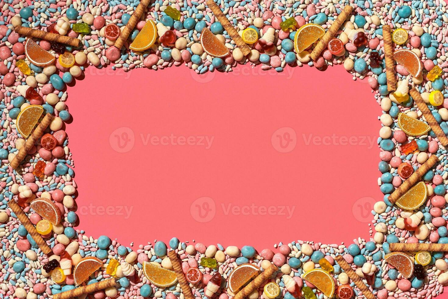 Multicolored glazed dragees and other sweets are arranged in the form of a frame on a coral background. photo