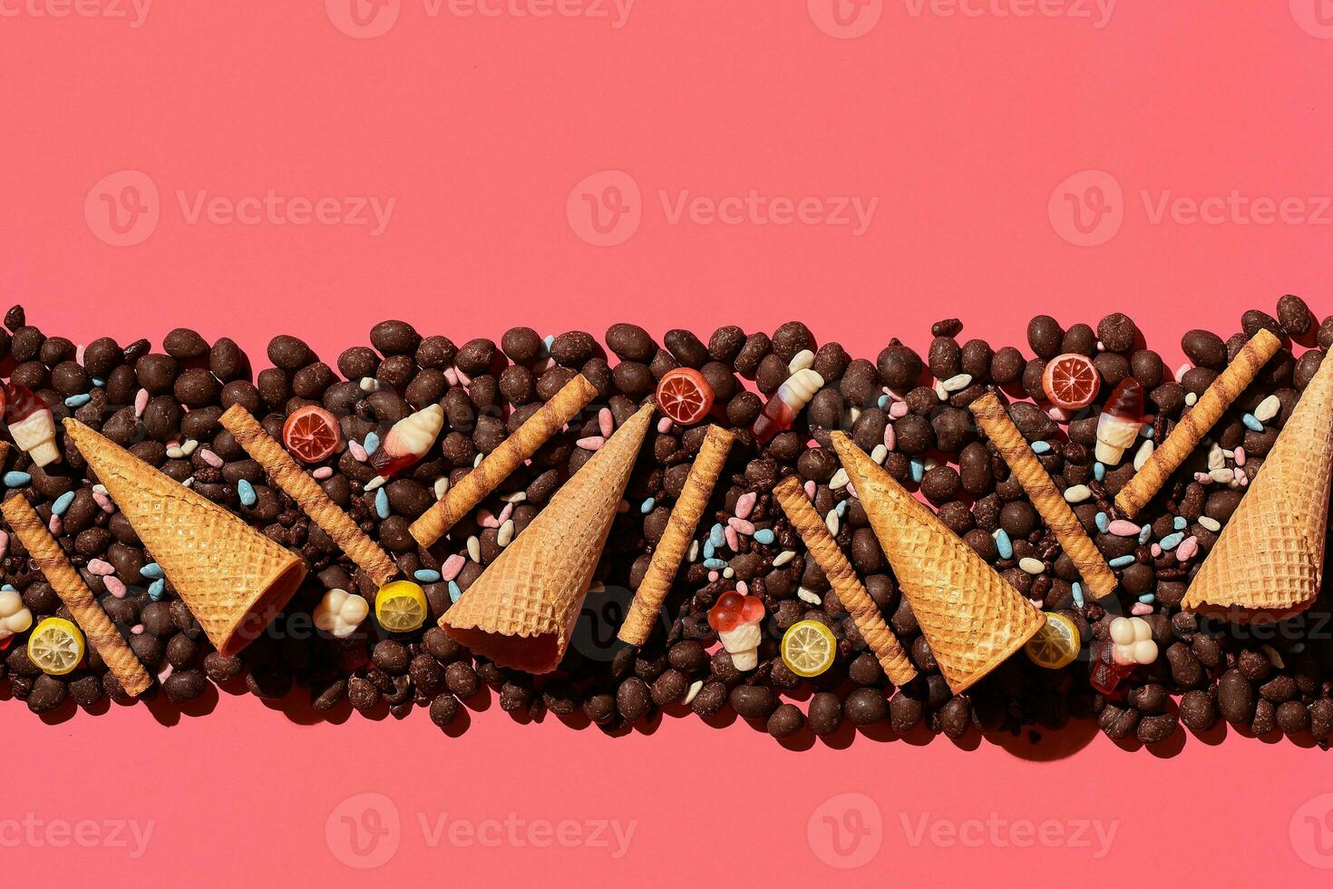 Chocolate dragee and waffle cones placed in fascinating order on coral background, view from above photo