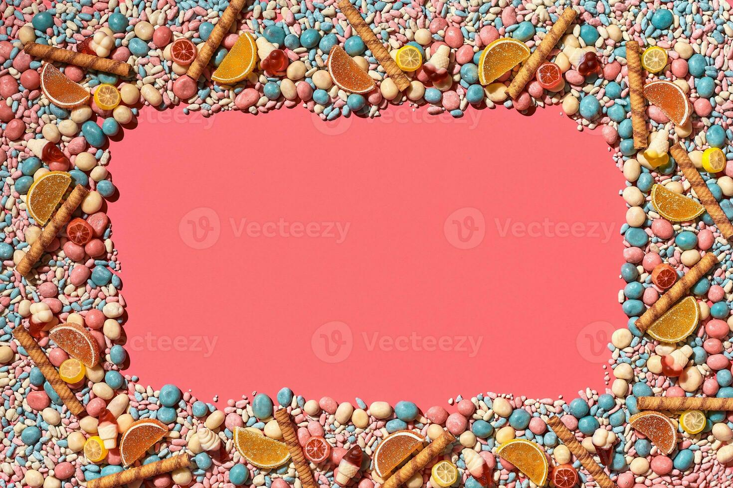 Multicolored glazed dragees and other sweets are arranged in the form of a frame on a coral background. photo