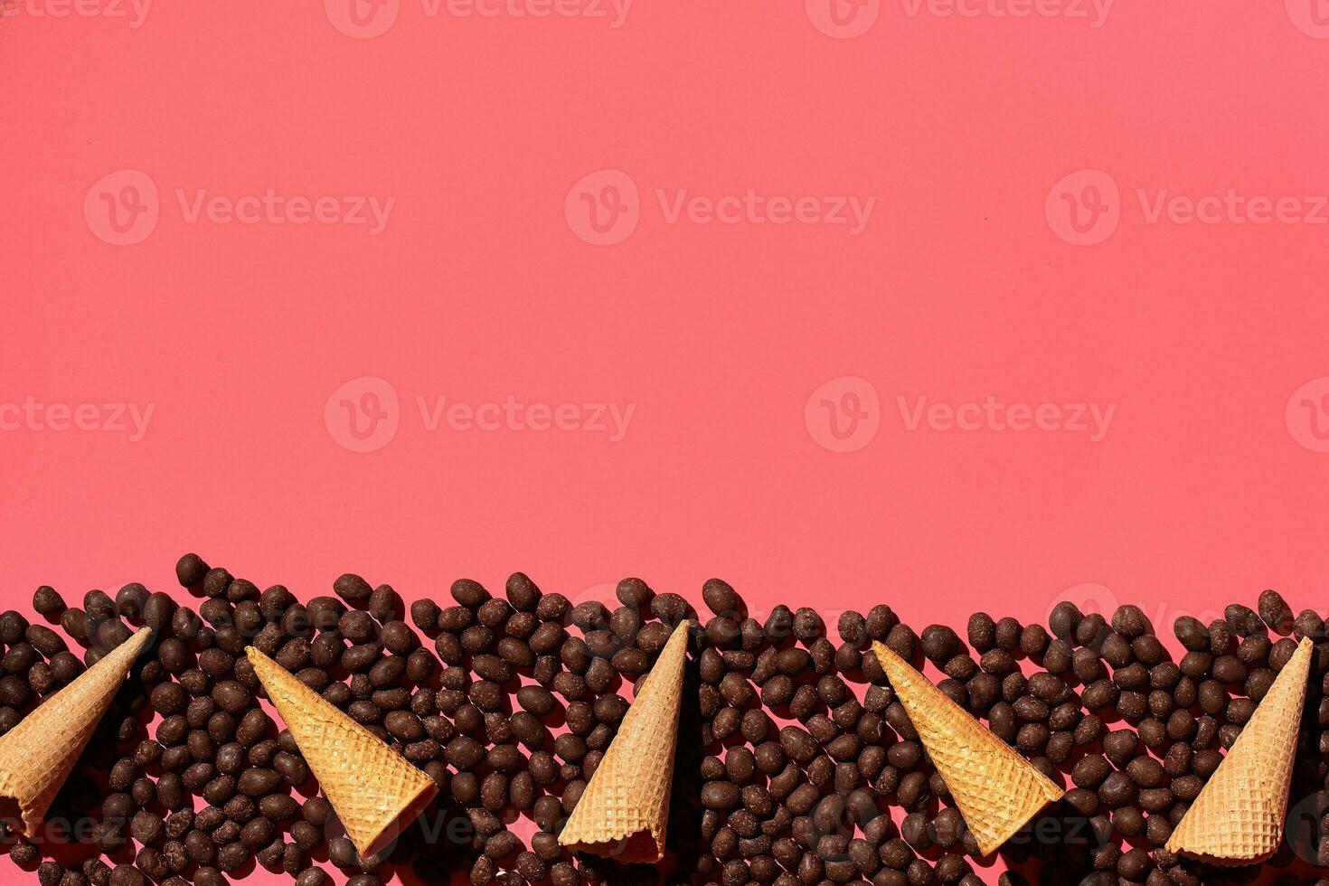 Chocolate dragee and waffle cones placed in fascinating order on coral background, view from above photo