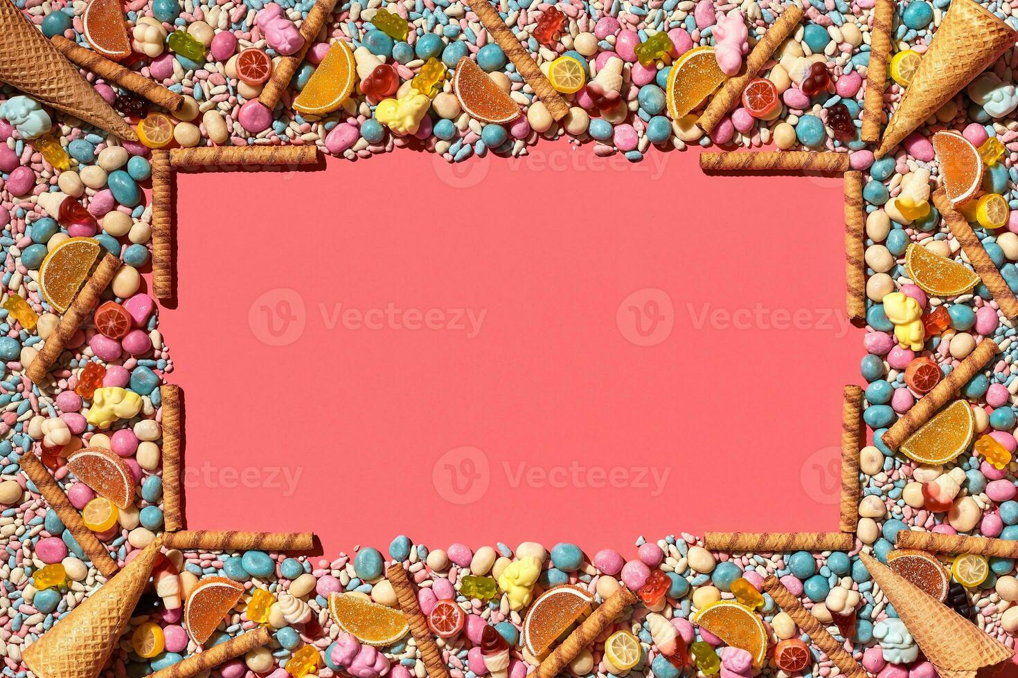 Multicolored glazed dragees and other sweets are arranged in the form of a frame on a coral background. photo