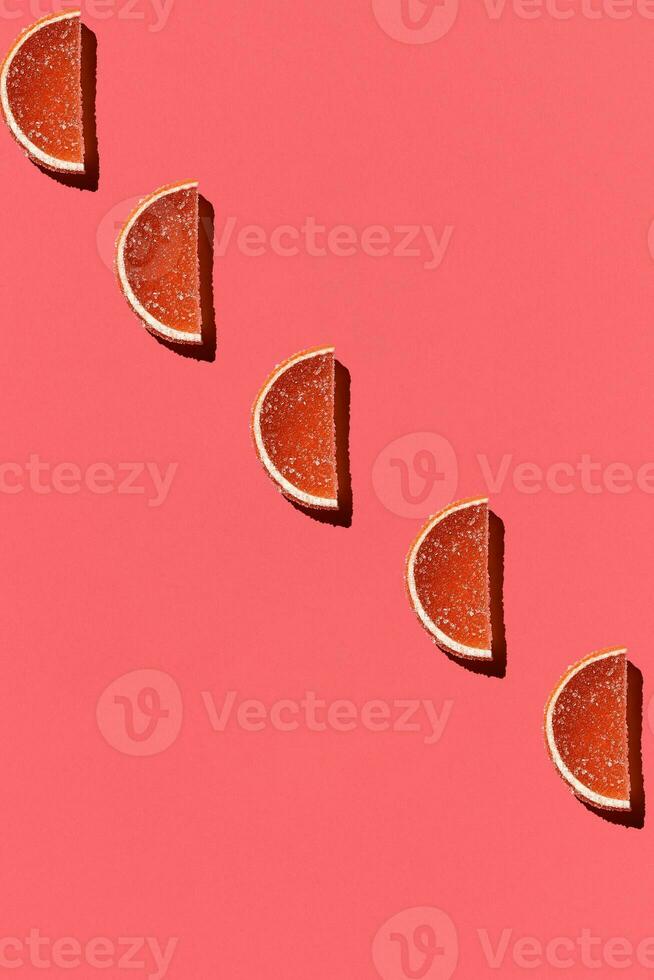 Pattern made of colorful candied fruits orange lemon on coral background. Flat lay. Minimal concept photo