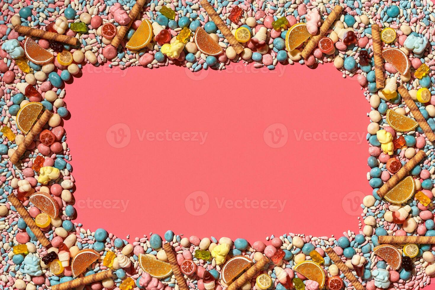 Multicolored glazed dragees and other sweets are arranged in the form of a frame on a coral background. photo