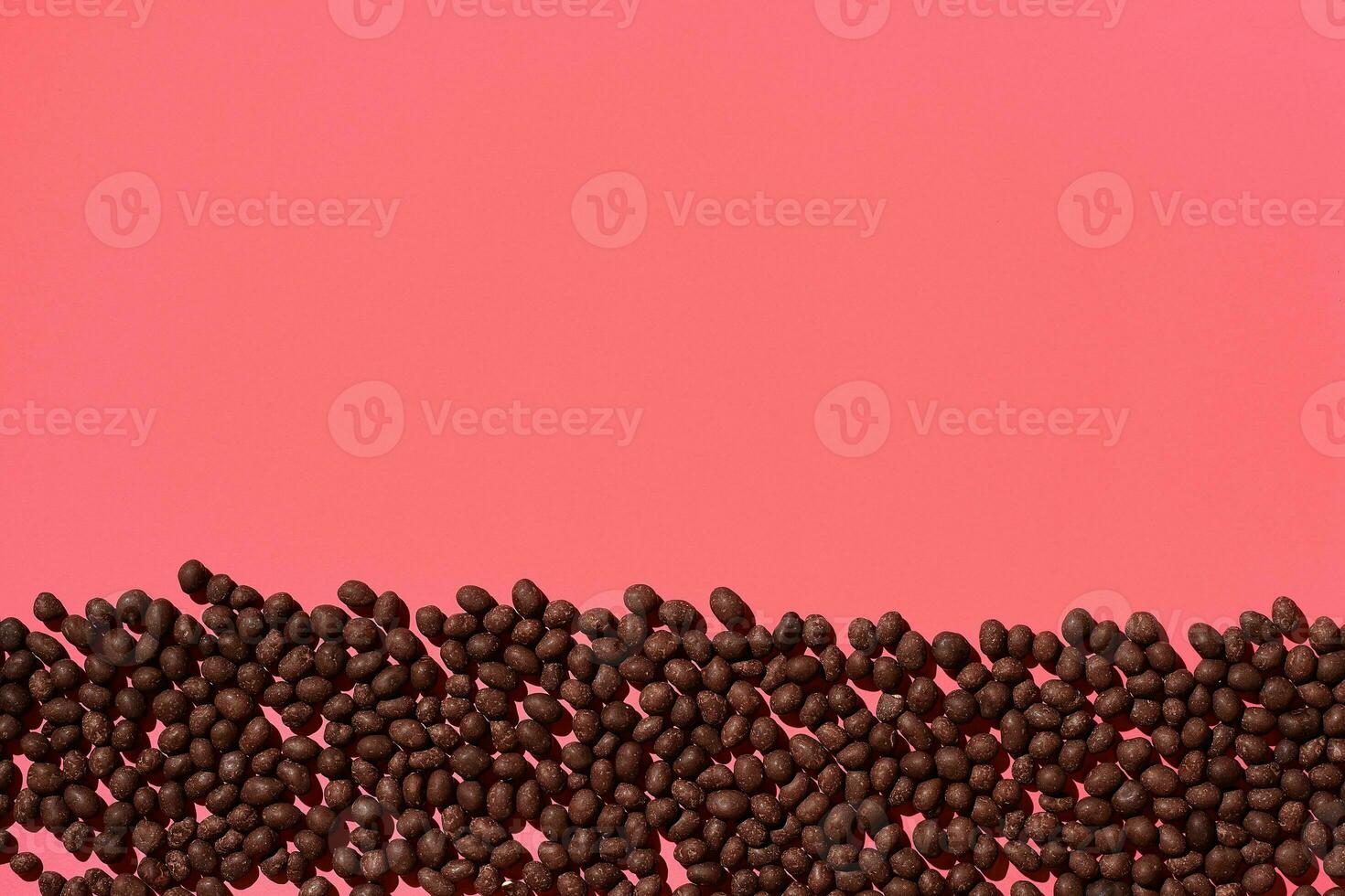 Chocolate dragee are placed in fascinating order on coral background, view from above photo