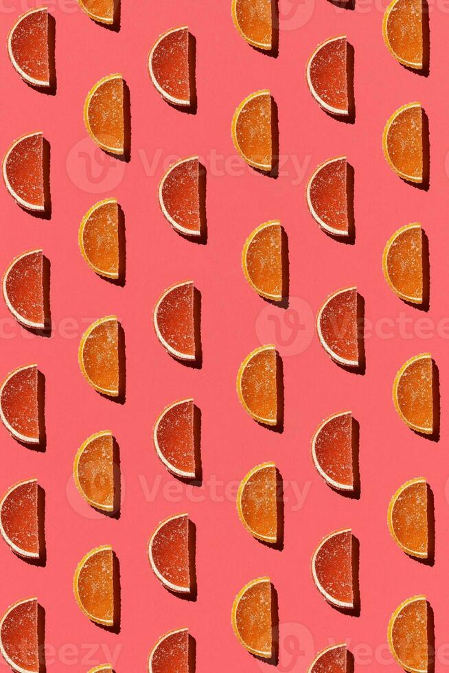 Pattern made of colorful candied fruits orange lemon on coral background. Flat lay. Minimal concept photo