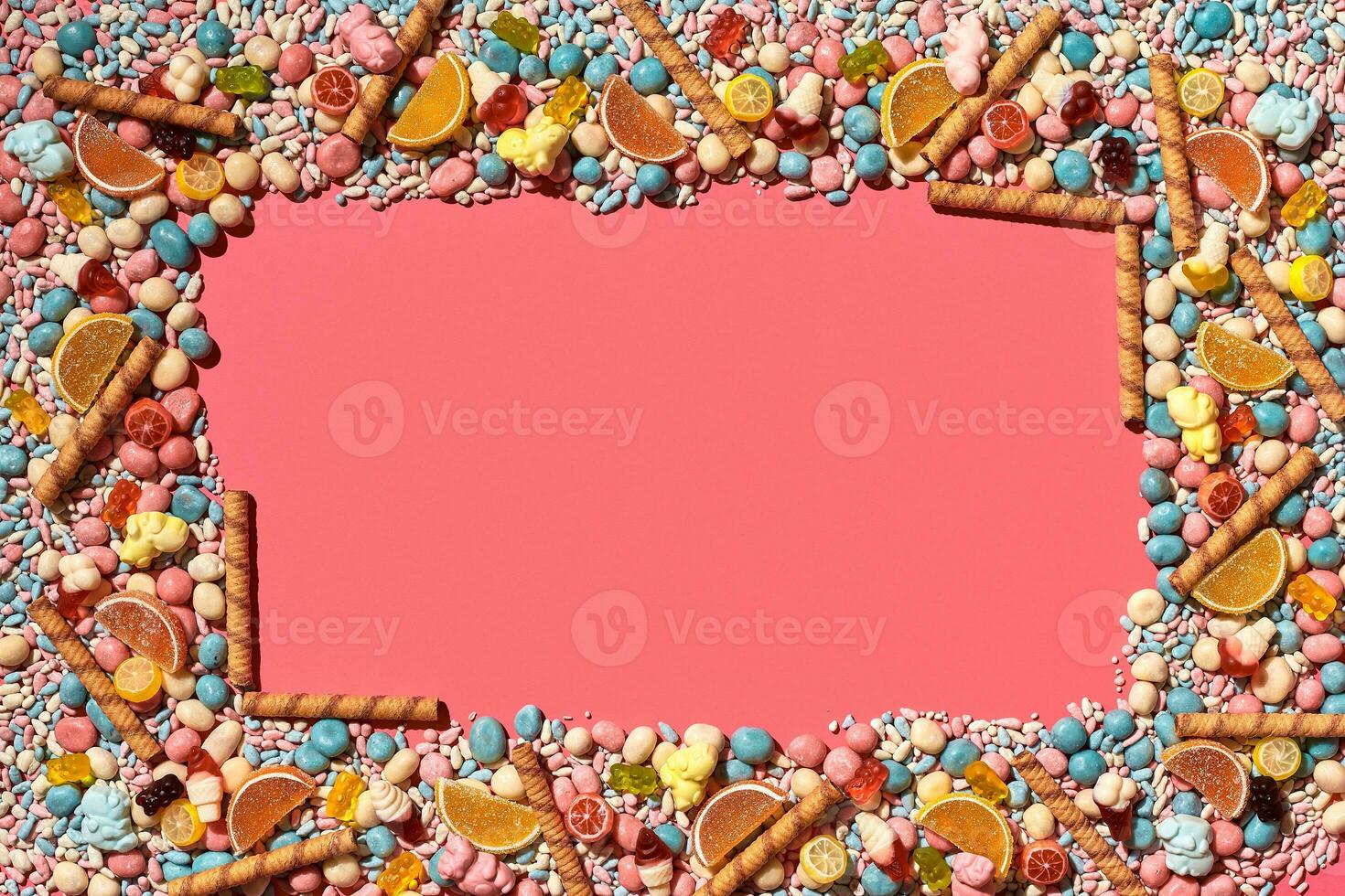Multicolored glazed dragees and other sweets are arranged in the form of a frame on a coral background. photo