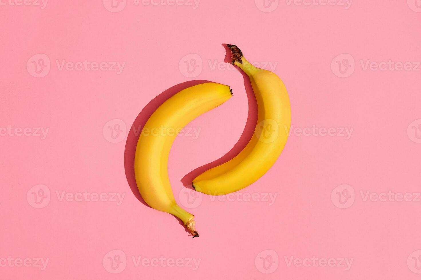Composition of a pair of bananas lying next to a pink background in the center of the image, top view photo