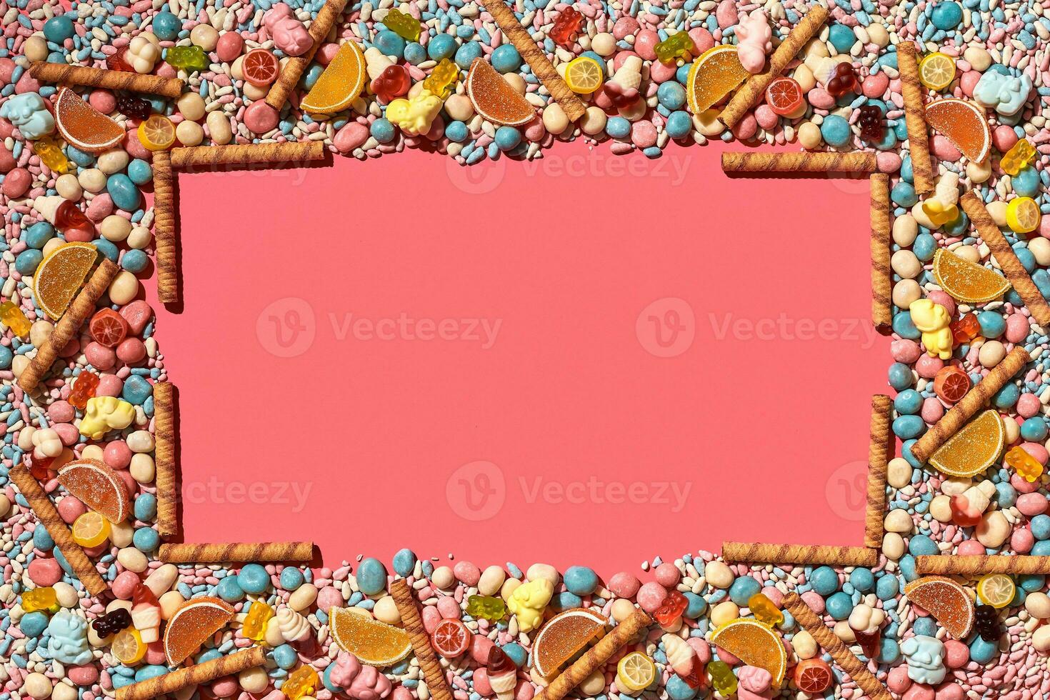 Multicolored glazed dragees and other sweets are arranged in the form of a frame on a coral background. photo