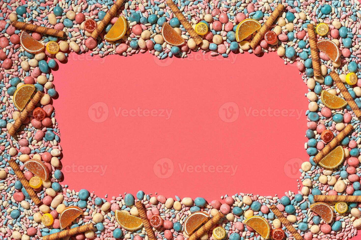 Multicolored glazed dragees and other sweets are arranged in the form of a frame on a coral background. photo