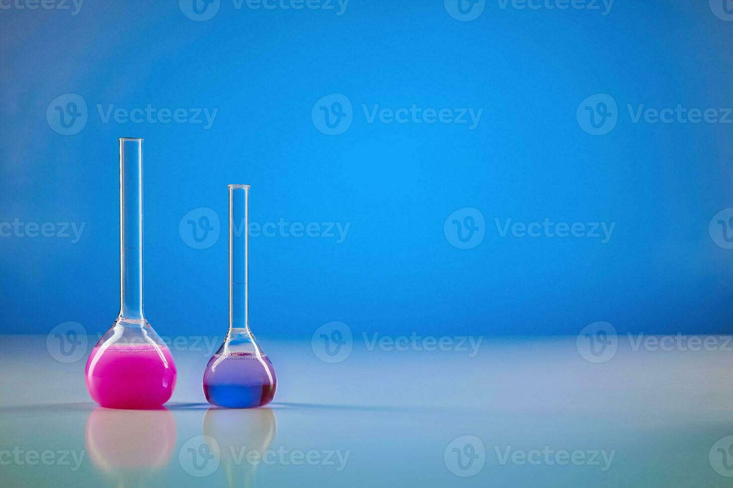 Two medical flasks with colorful chemical reagents for tests, blue background. Laboratory research of Coronavirus. Pandemic COVID-19. Close up photo