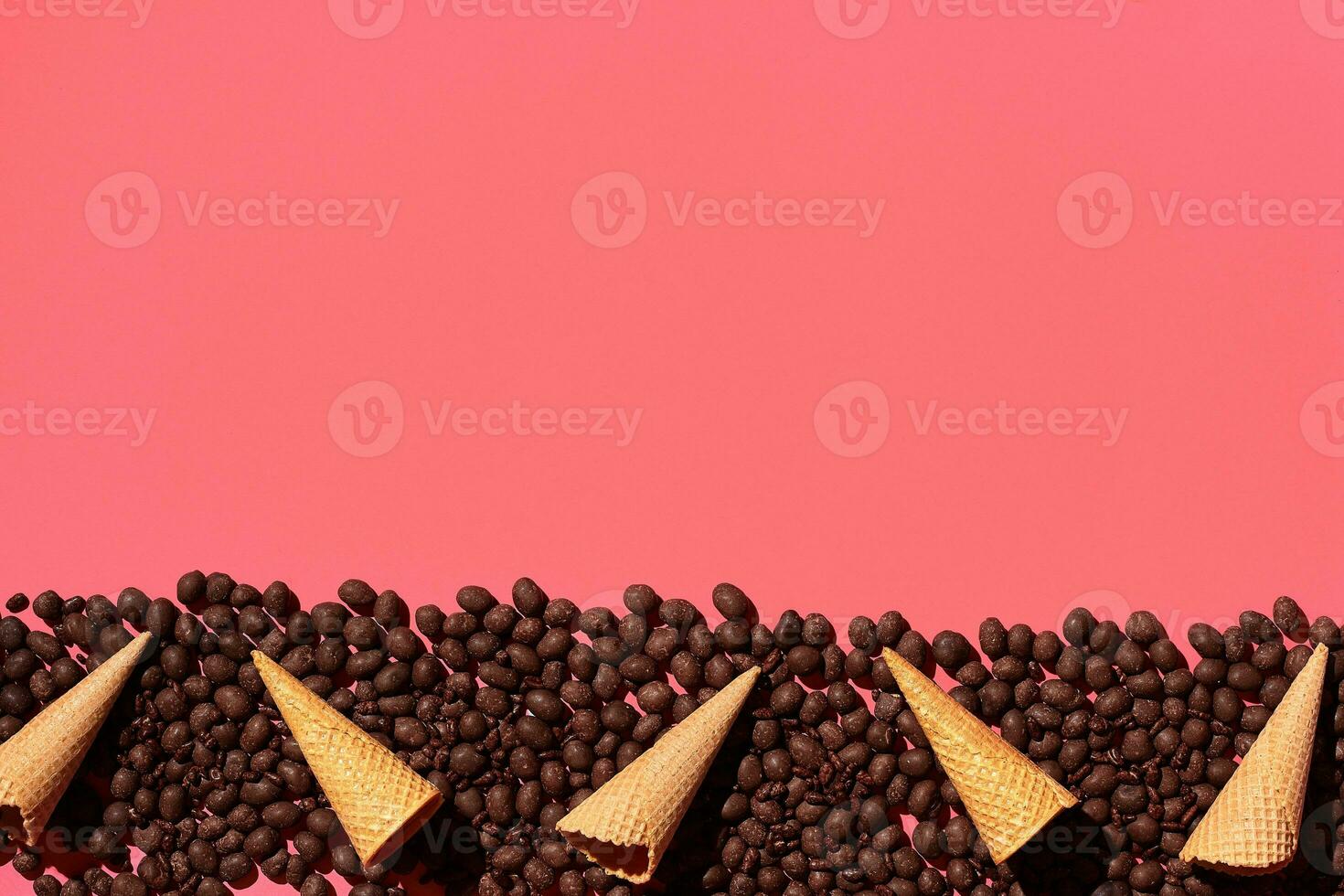 Chocolate dragee and waffle cones placed in fascinating order on coral background, view from above photo