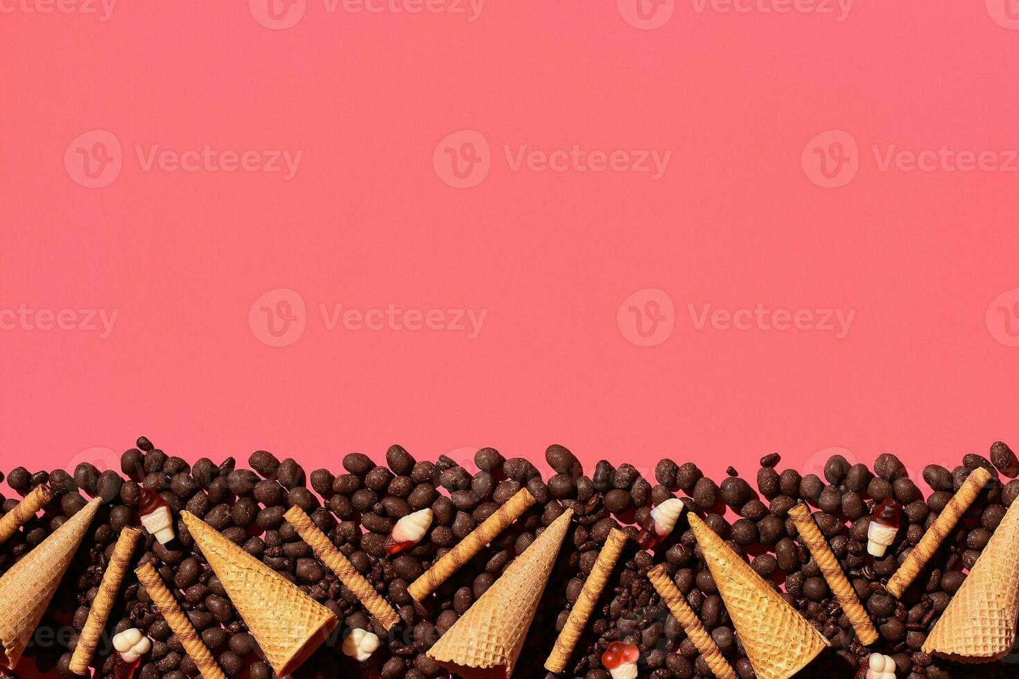 Chocolate dragee and waffle cones placed in fascinating order on coral background, view from above photo