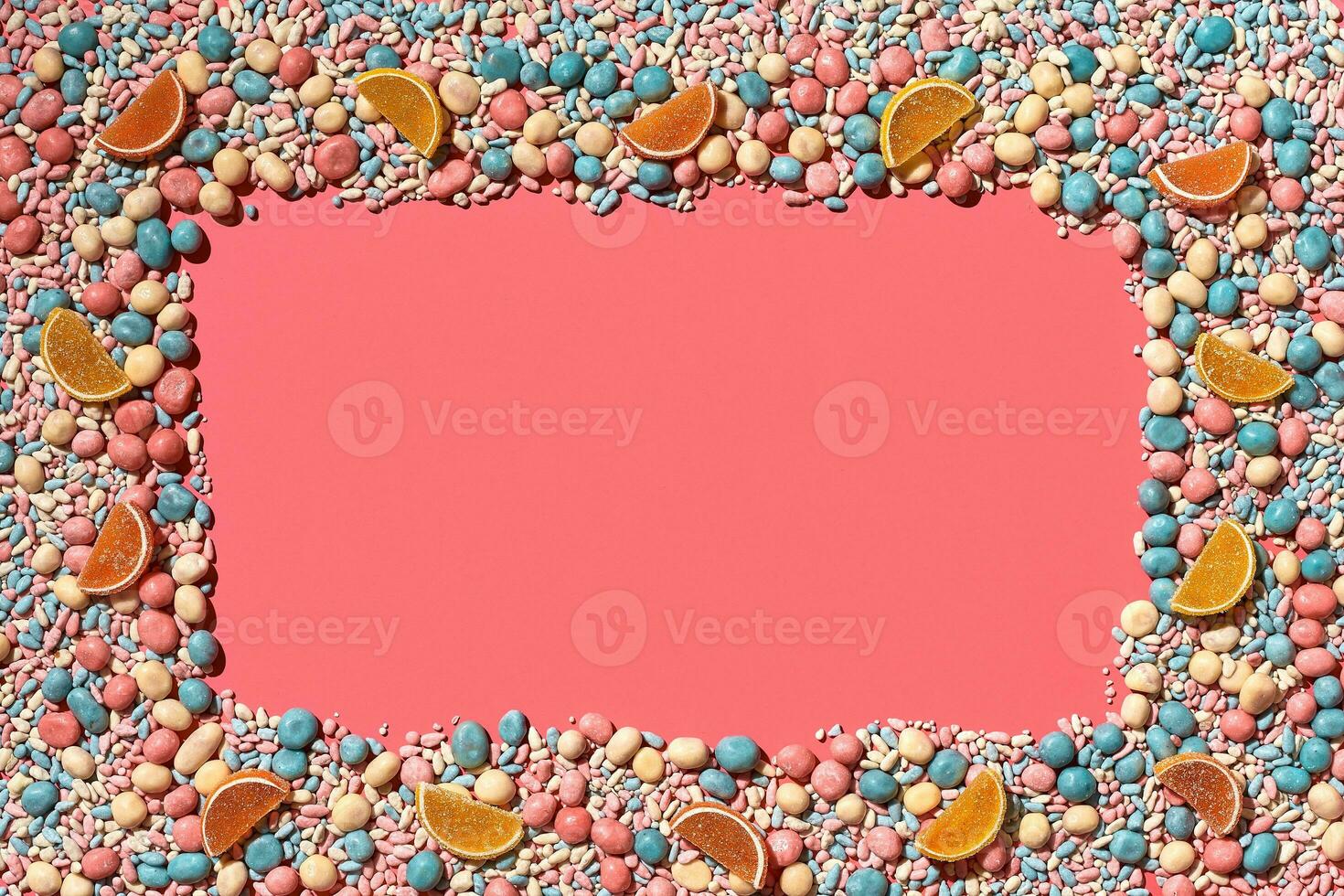 Multicolored glazed dragees and other sweets are arranged in the form of a frame on a coral background. photo