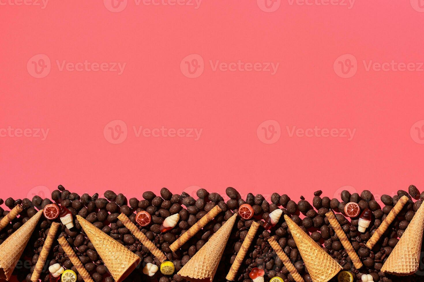 Chocolate dragee and waffle cones placed in fascinating order on coral background, view from above photo
