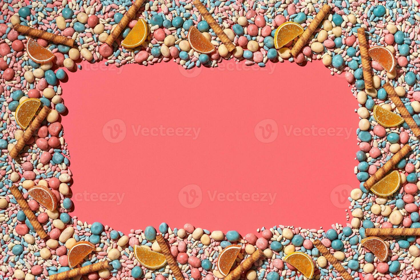 Multicolored glazed dragees and other sweets are arranged in the form of a frame on a coral background. photo