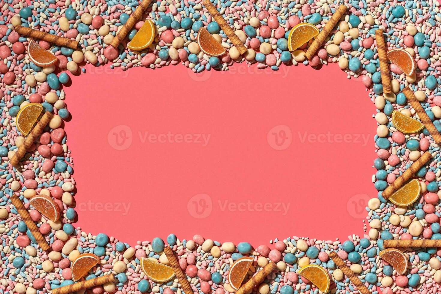 Multicolored glazed dragees and other sweets are arranged in the form of a frame on a coral background. photo