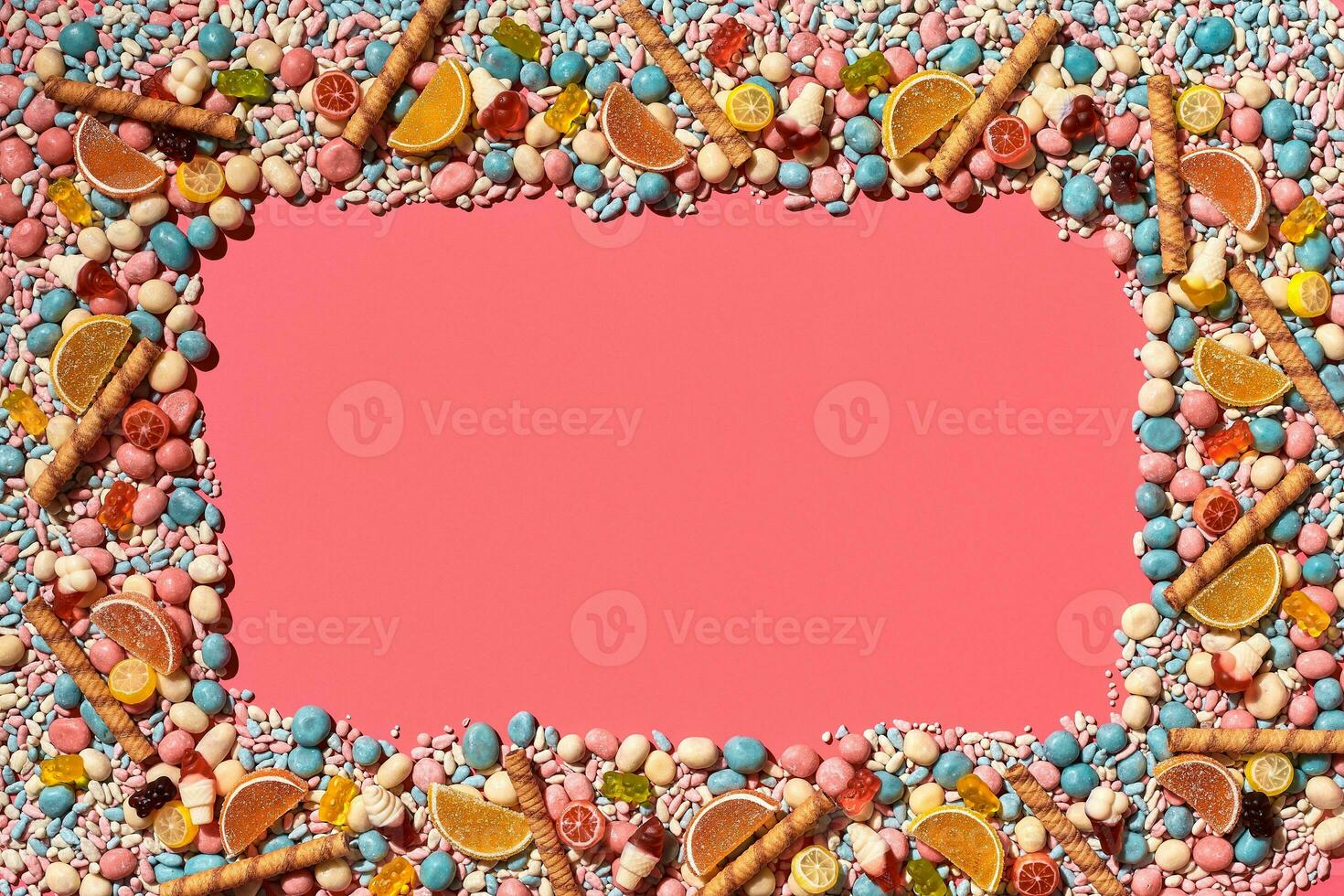 Multicolored glazed dragees and other sweets are arranged in the form of a frame on a coral background. photo