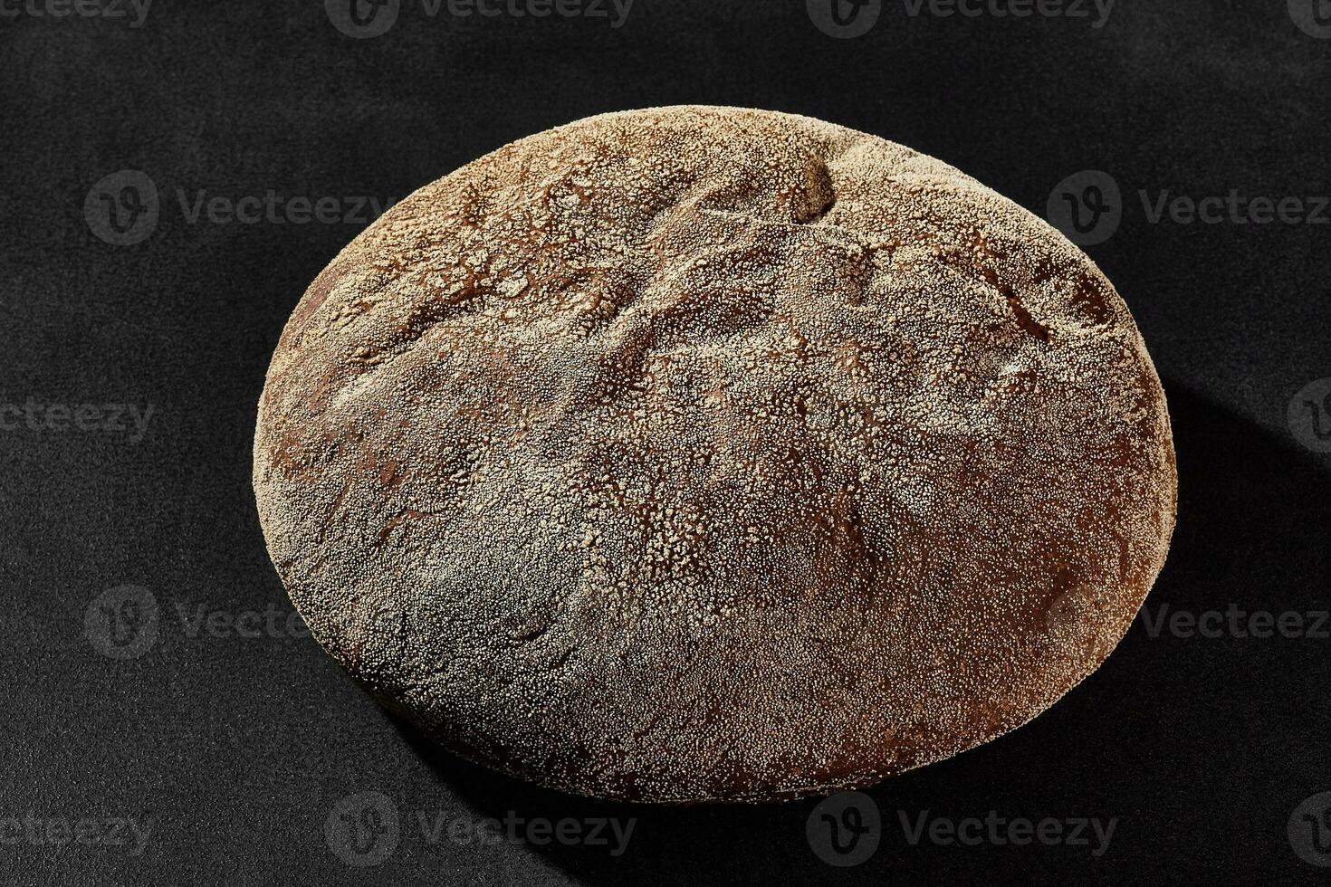 Fresh, tasty baked round dark bread sprinkled with flour. Black background with copy space. Rural cuisine or bakery. Close-up photo