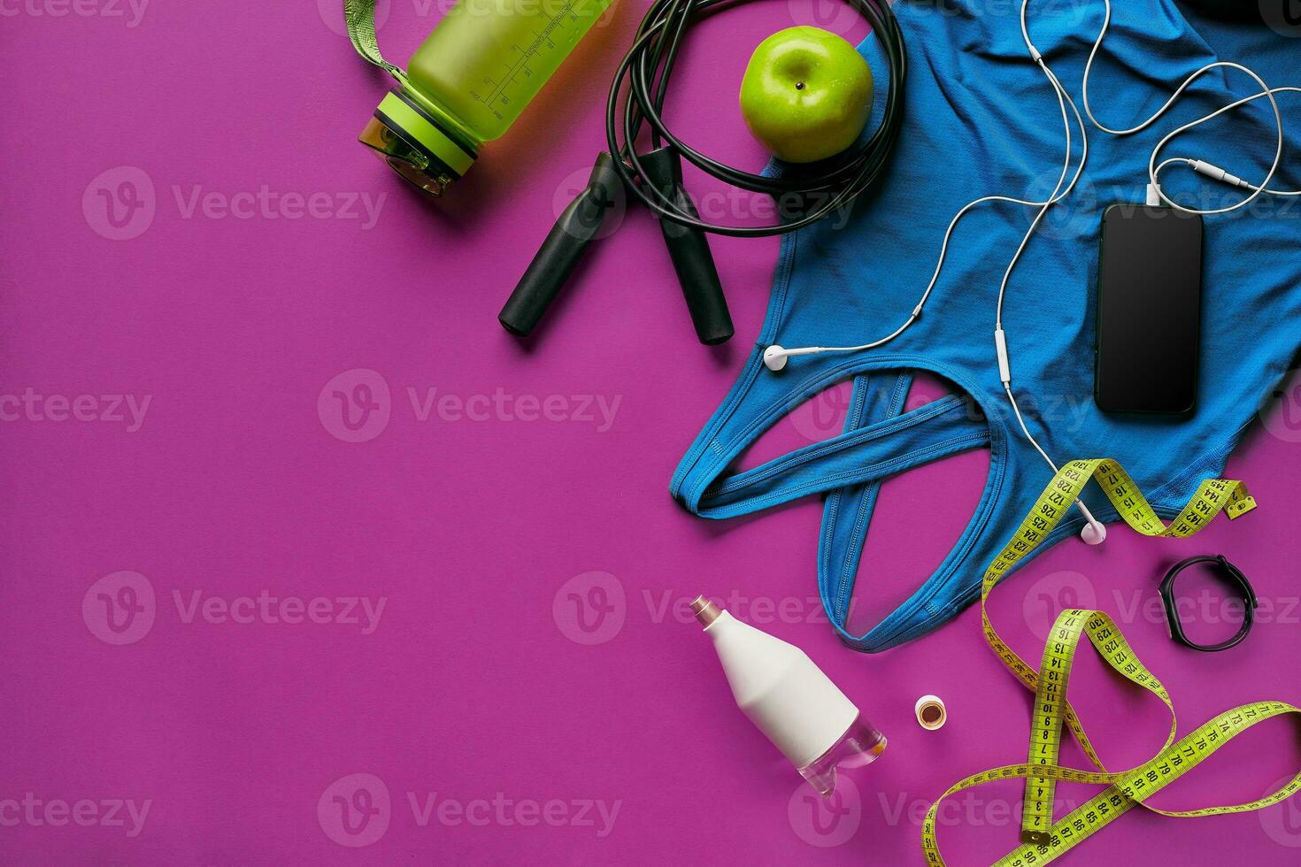 Health fitness background. Sneakers, dumbbell, power grip, green apple, water bottle, blue shirt, phone and earphone on dark background. photo