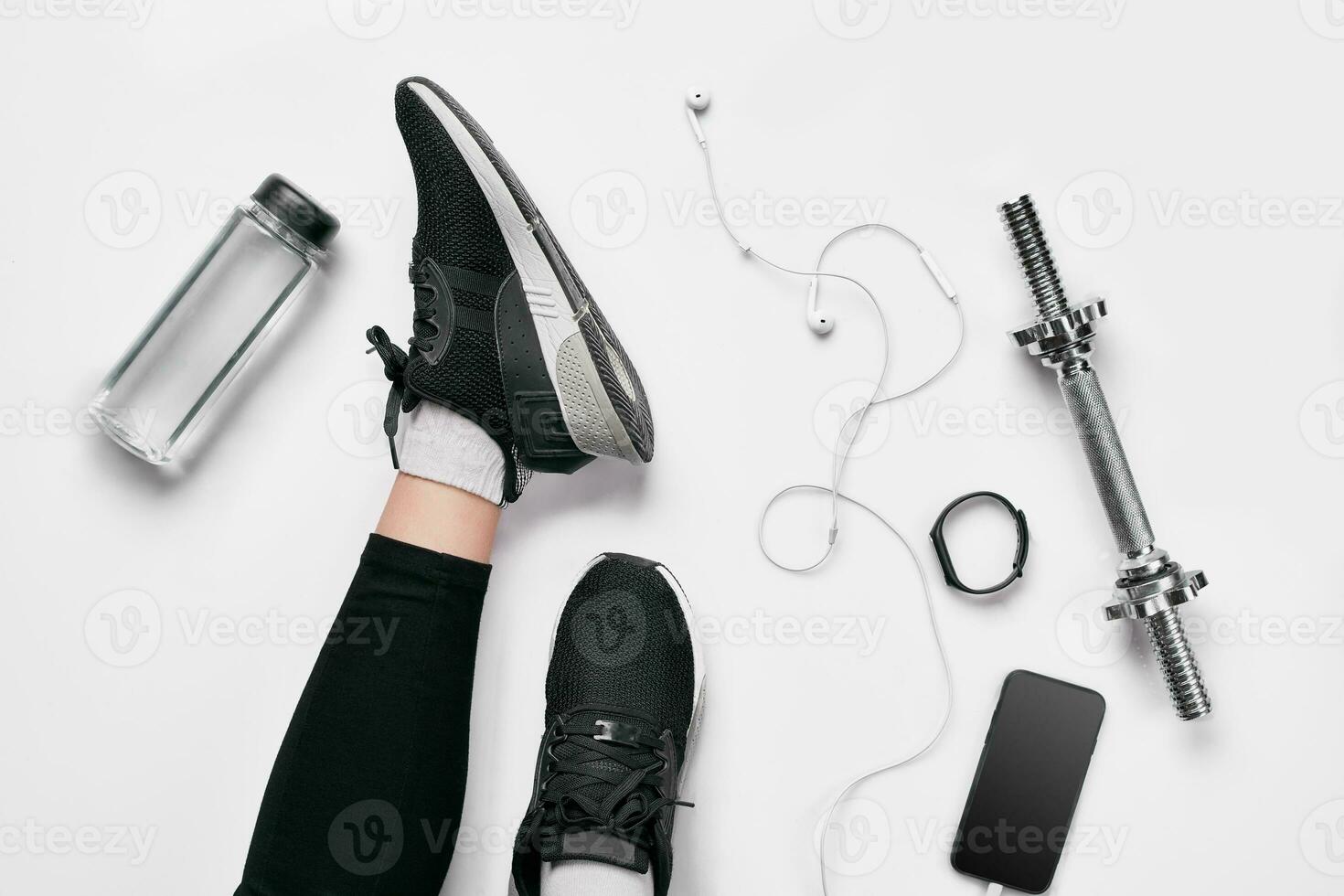 Women's legs in sneakers, fitness clothing, smartphone, dumbbells, headphones, top view. photo