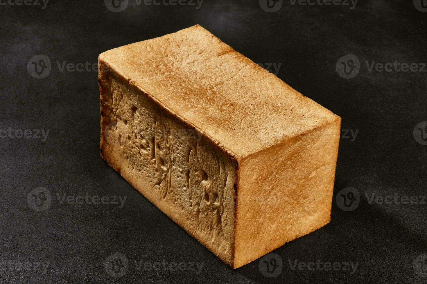 Whole loaf of fresh, delicious baked white bread against black background with copy space. Close-up photo