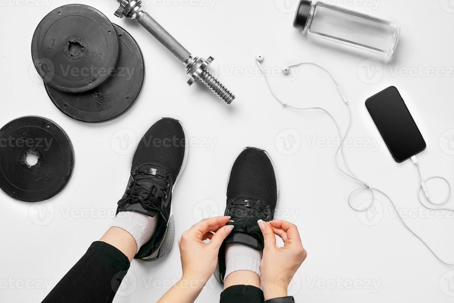 Young woman in sporting leggings laces sneakers, preparing for training. Accessories for sports on white background flat lay top view. photo