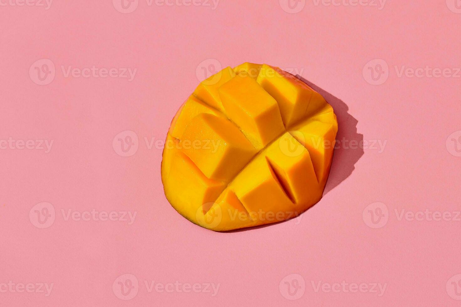 Colorful fruit pattern of fresh juicy cutted mango laying on the middle of the image on coral pink background, top view photo