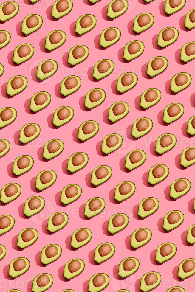 Colorful fruit pattern of fresh cutted avocado halves with pits on coral pink background, top view photo