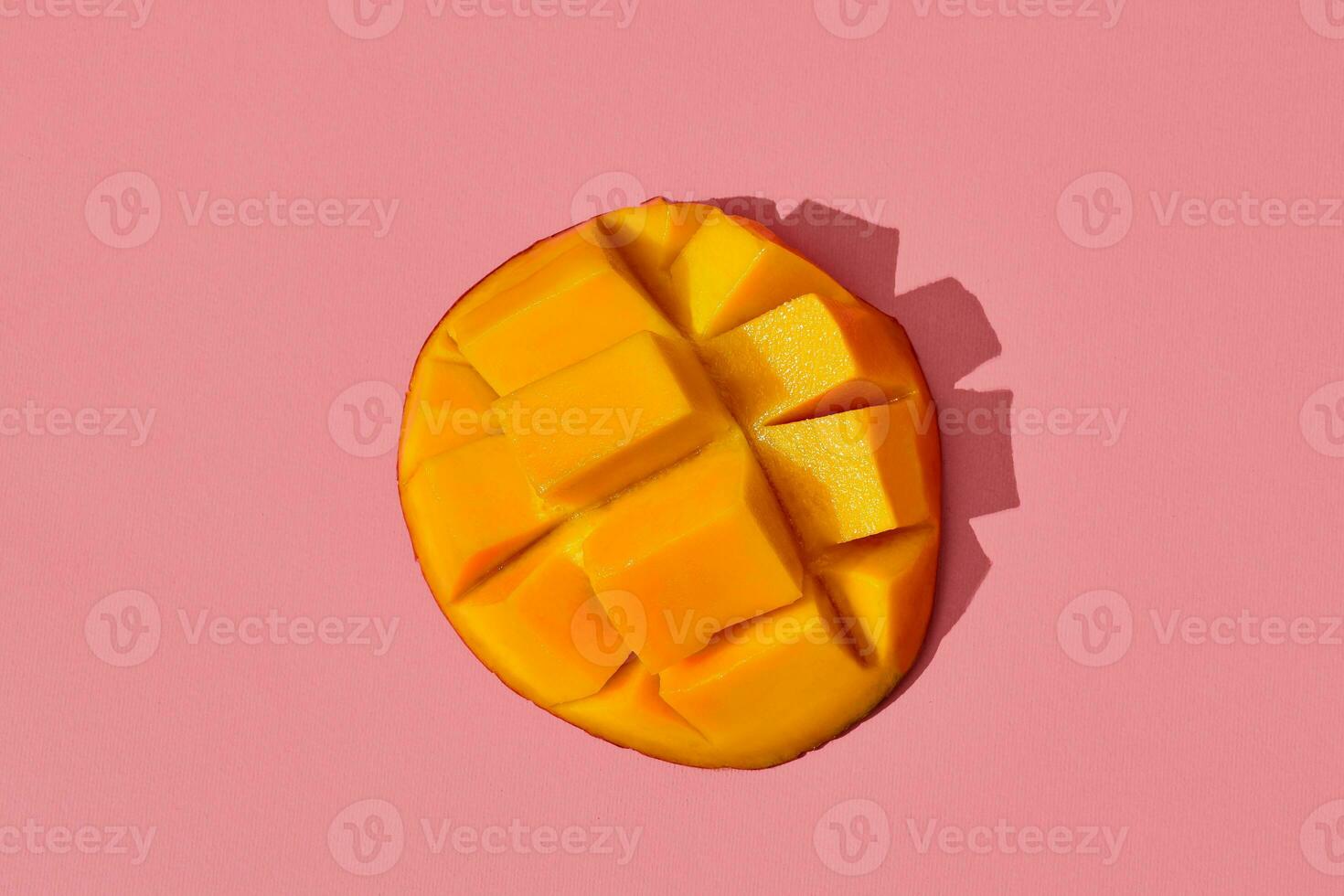 Colorful fruit pattern of fresh juicy cutted mango laying on the middle of the image on coral pink background, top view photo