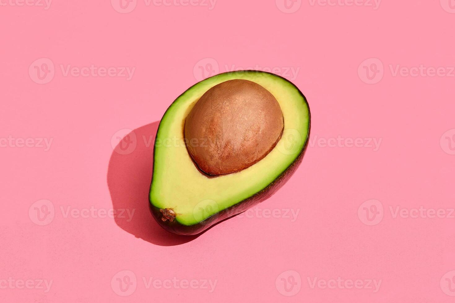 Colorful fruit pattern of fresh cutted avocado halve with pit on coral pink background, top view photo