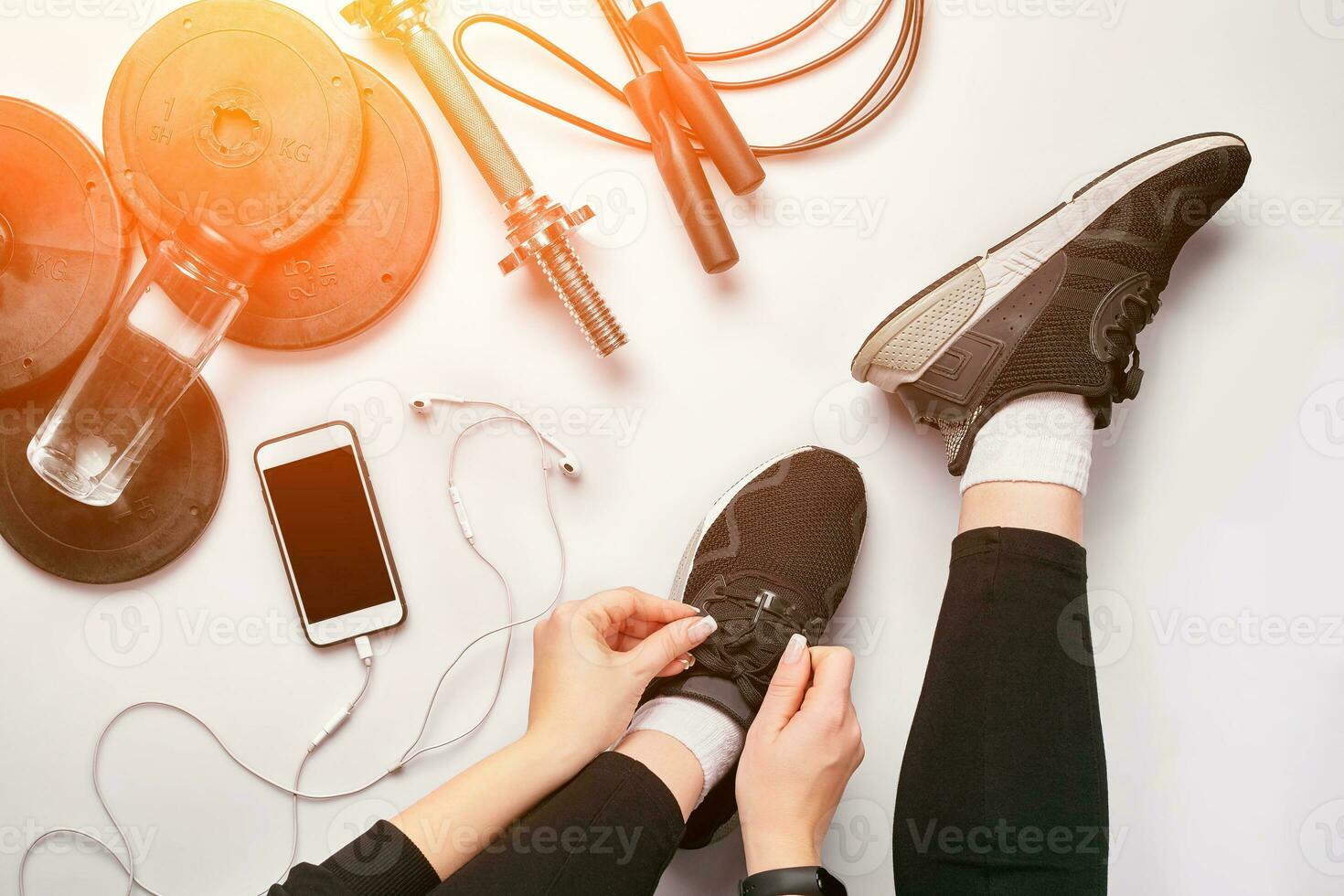 Young woman in sporting leggings laces sneakers, preparing for training. Accessories for sports on white background flat lay top view. photo