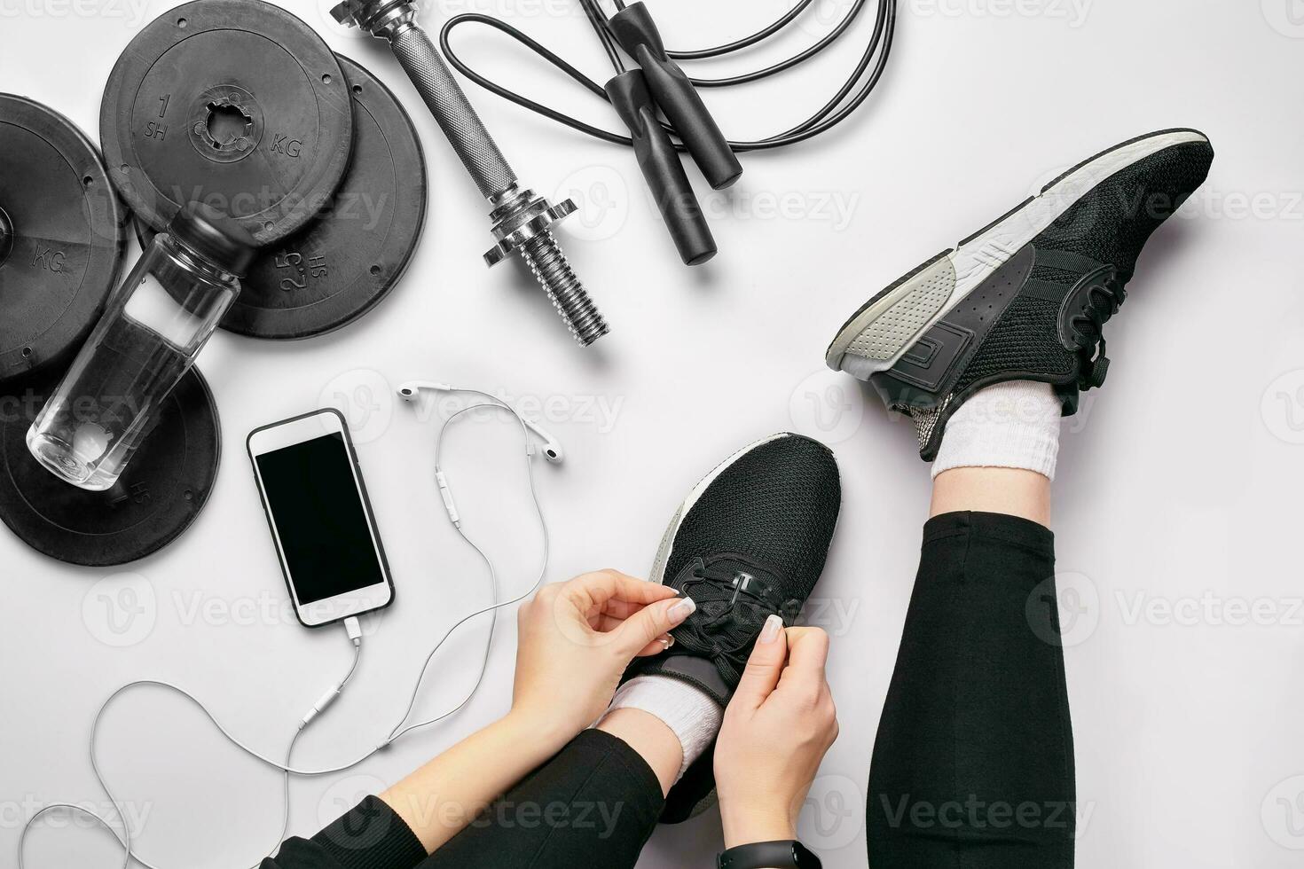 Young woman in sporting leggings laces sneakers, preparing for training. Accessories for sports on white background flat lay top view. photo