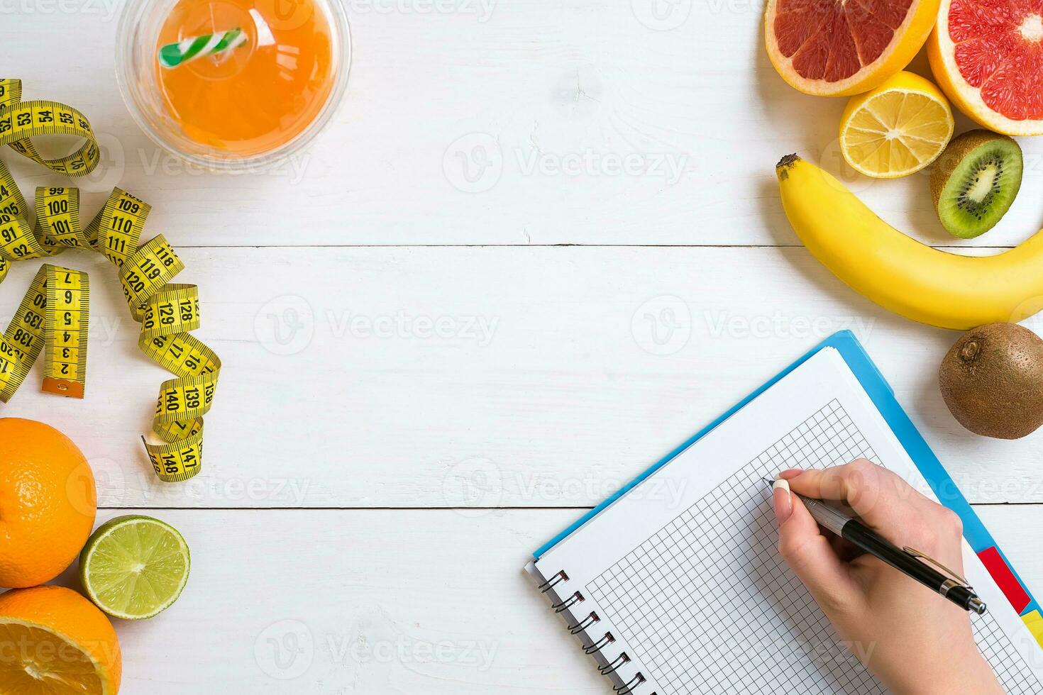 Fresh juice in glass from citrus fruits - lemon, grapefruit, orange, notebook with pencil on white wooden background photo