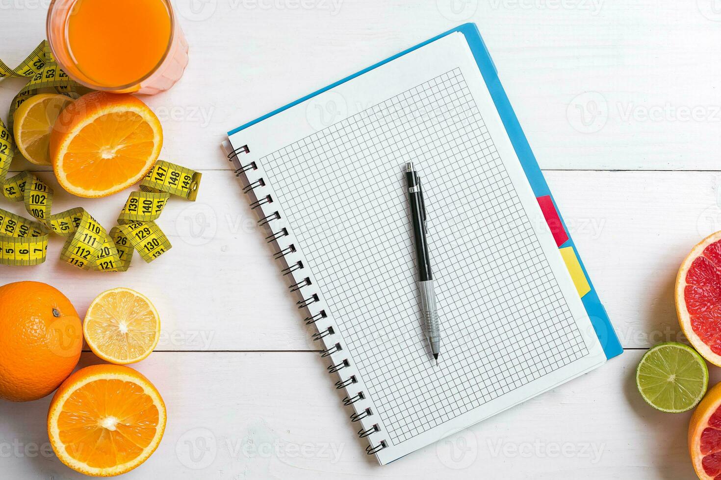 Fresh juice in glass from citrus fruits - lemon, grapefruit, orange, notebook with pencil on white wooden background photo