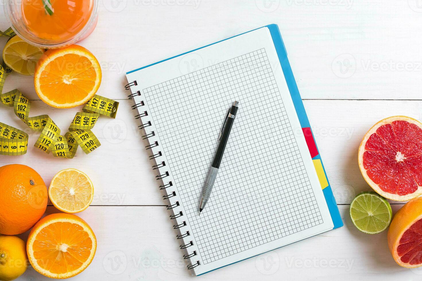 Fresh juice in glass from citrus fruits - lemon, grapefruit, orange, notebook with pencil on white wooden background photo