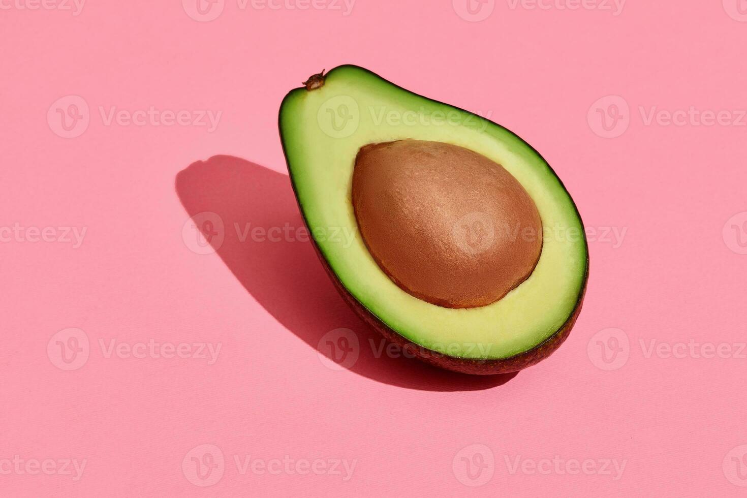 Colorful fruit pattern of fresh cutted avocado halve with pit on coral pink background, top view photo