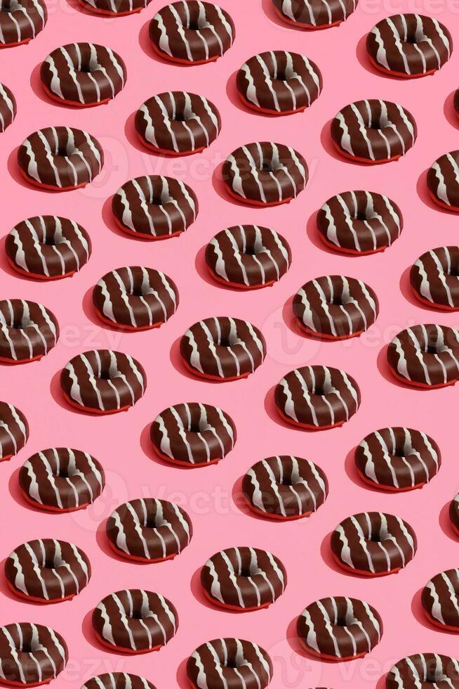 Food design with tasty chocolate glazed donut with white strips on coral pink pastel background top view pattern photo