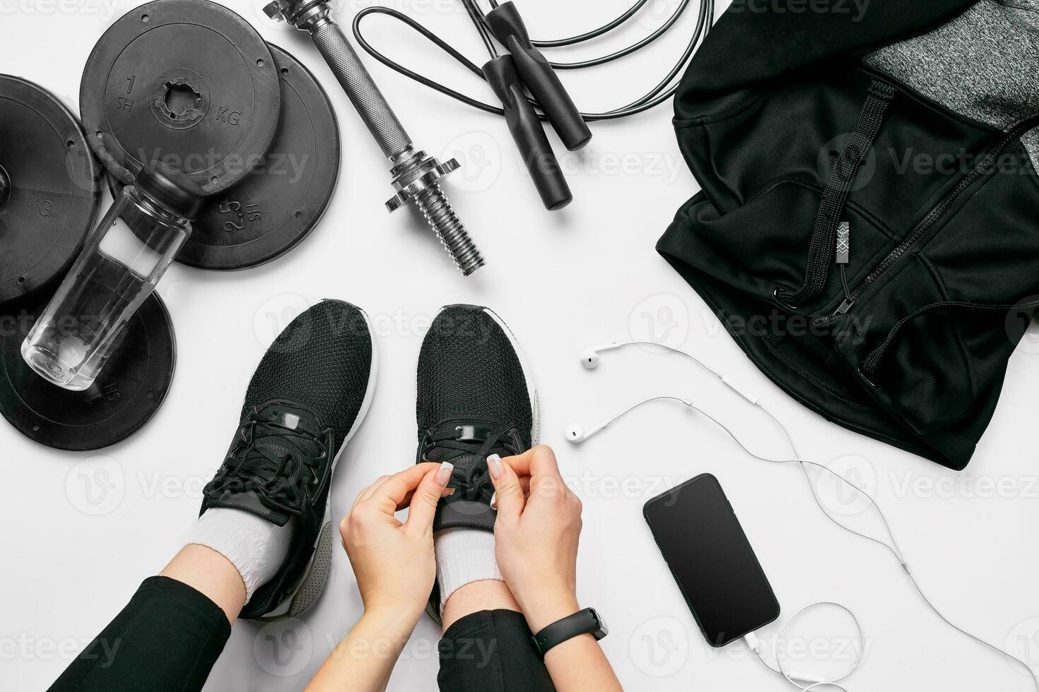 Young woman in sporting leggings laces sneakers, preparing for training. Accessories for sports on white background flat lay top view. photo