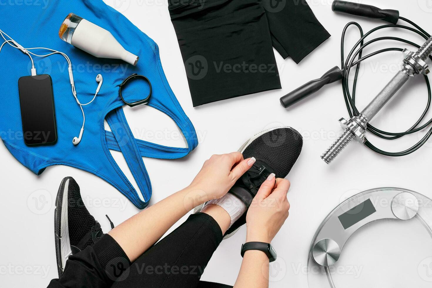 Young woman in sporting leggings laces sneakers, preparing for training. Accessories for sports on white background flat lay top view. photo