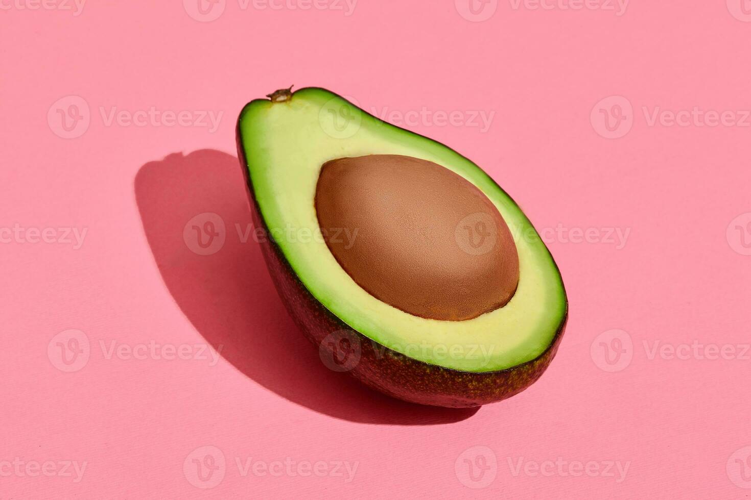 Colorful fruit pattern of fresh cutted avocado halve with pit on coral pink background, top view photo