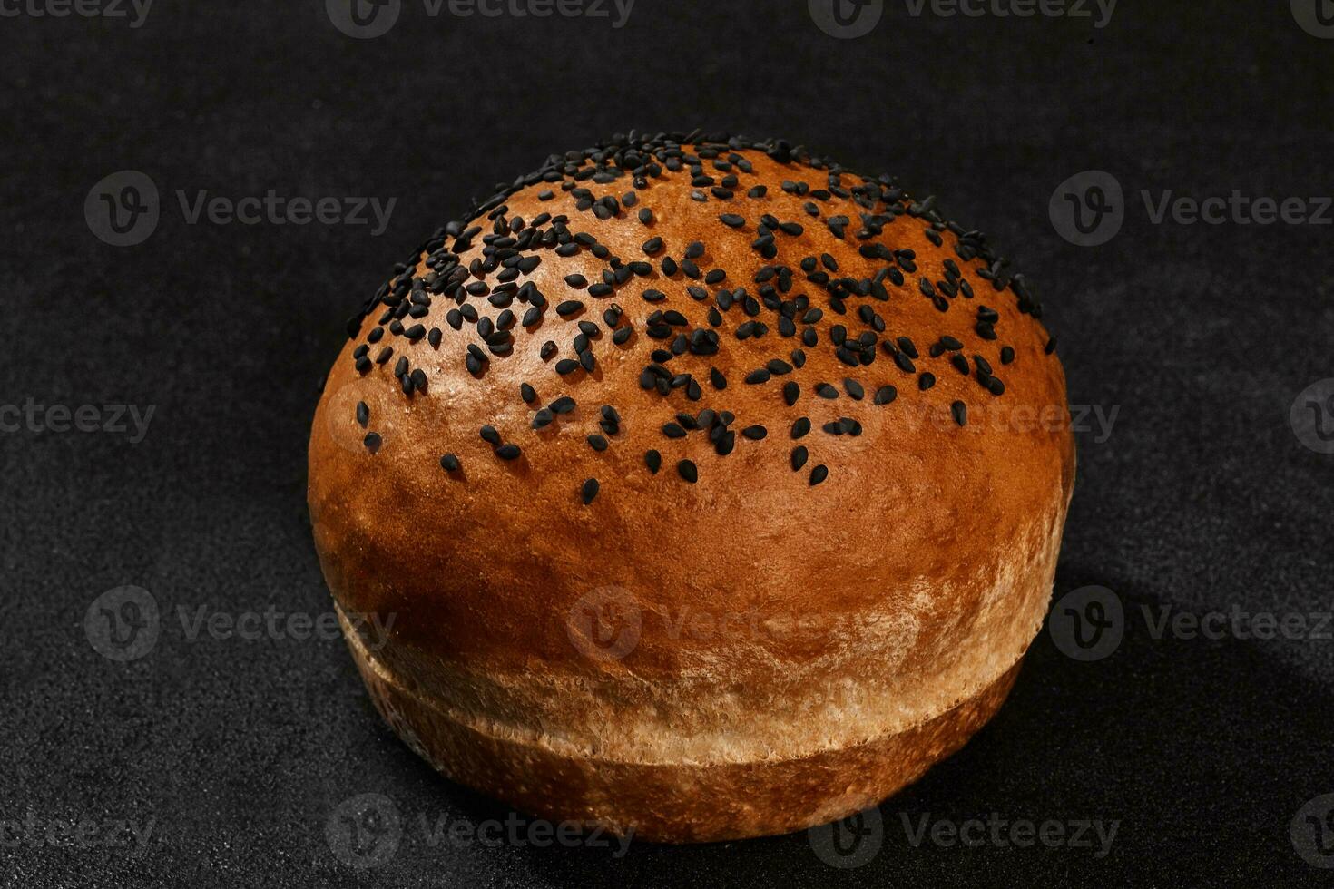 Fresh, palatable baked bun sprinkled with sesame seeds against black background with copy space. Rural cuisine or bakery. Close-up photo