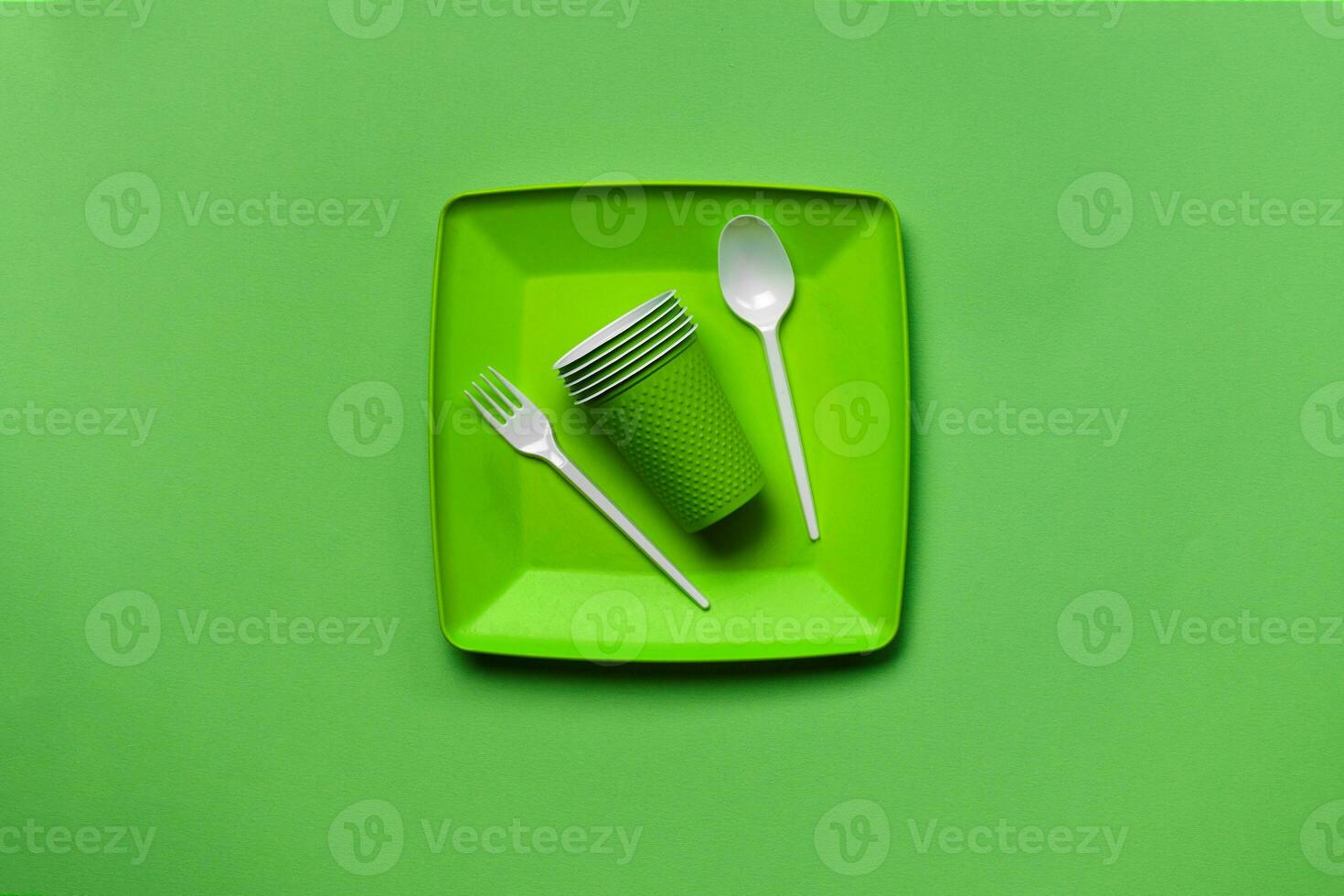 Colorful plastic disposable tableware on green background with copy space. The concept of picnic utensil. Top view. Selective focus. Close-up. photo