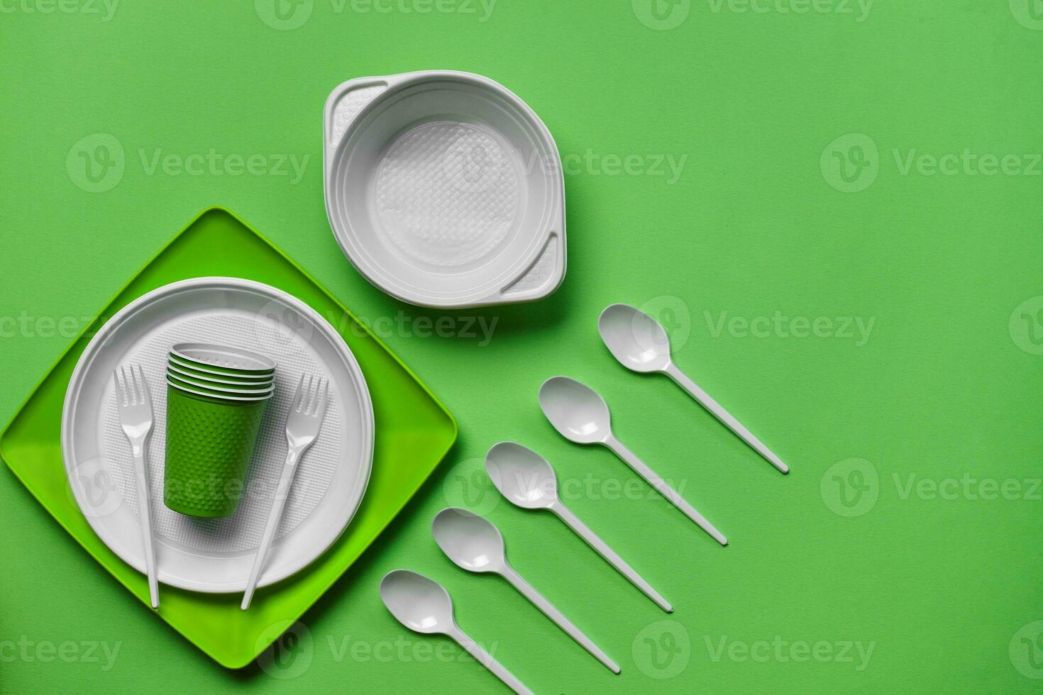 Colorful plastic disposable tableware on green background with copy space. The concept of picnic utensil. Top view. Selective focus. Close-up. photo