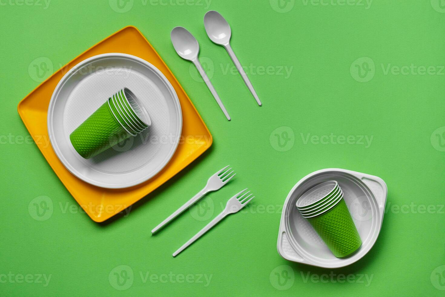 Colorful plastic disposable tableware on green background with copy space. The concept of picnic utensil. Top view. Selective focus. Close-up. photo