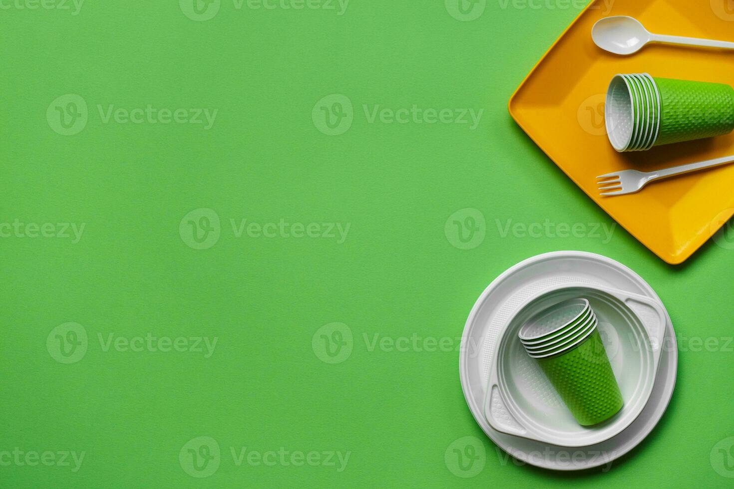 Colorful plastic disposable tableware on green background with copy space. The concept of picnic utensil. Top view. Selective focus. Close-up. photo