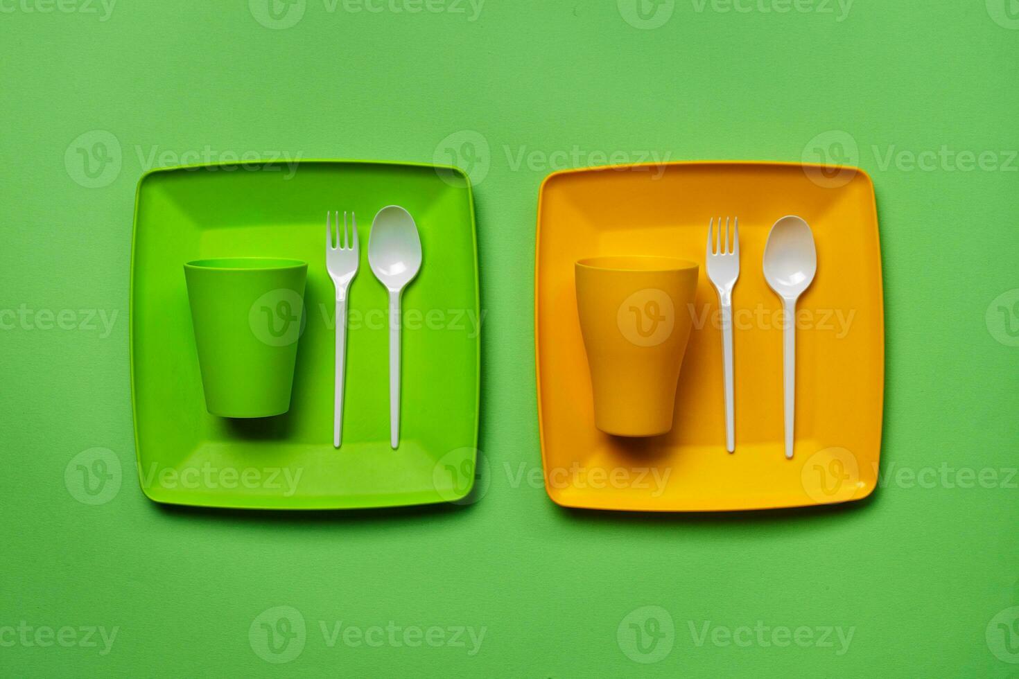 Colorful plastic disposable tableware on green background with copy space. The concept of picnic utensil. Top view. Selective focus. Close-up. photo