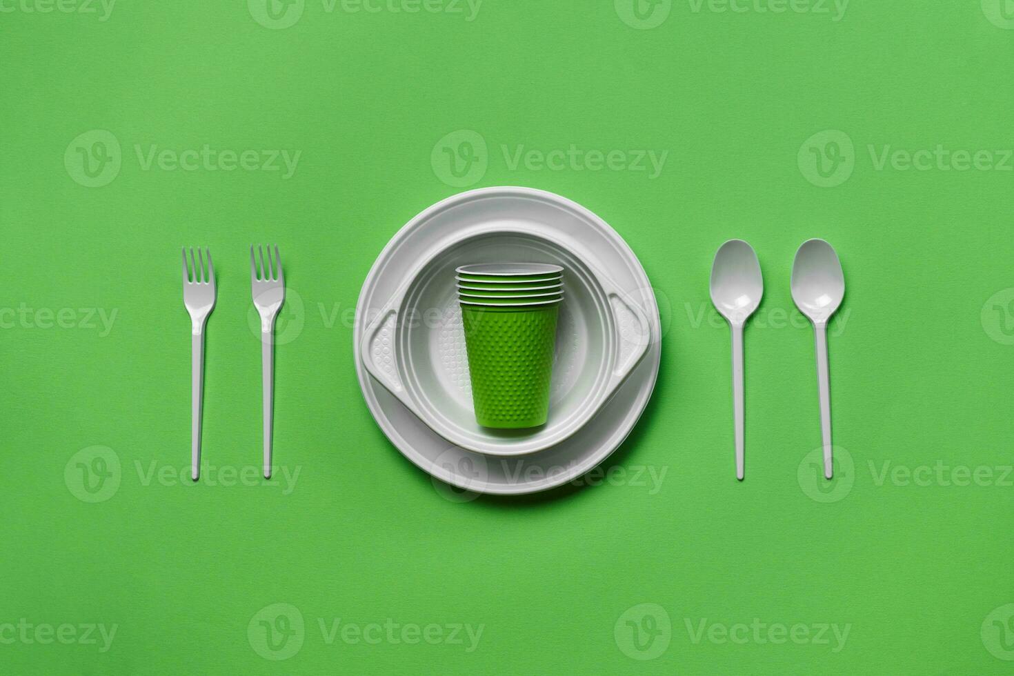 Colorful plastic disposable tableware on green background with copy space. The concept of picnic utensil. Top view. Selective focus. Close-up. photo