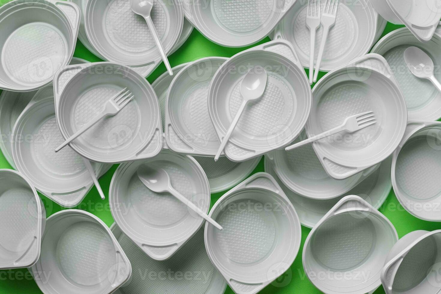 White plastic disposable tableware on green background with copy space. The concept of picnic utensil. Top view. Selective focus. Close-up. photo