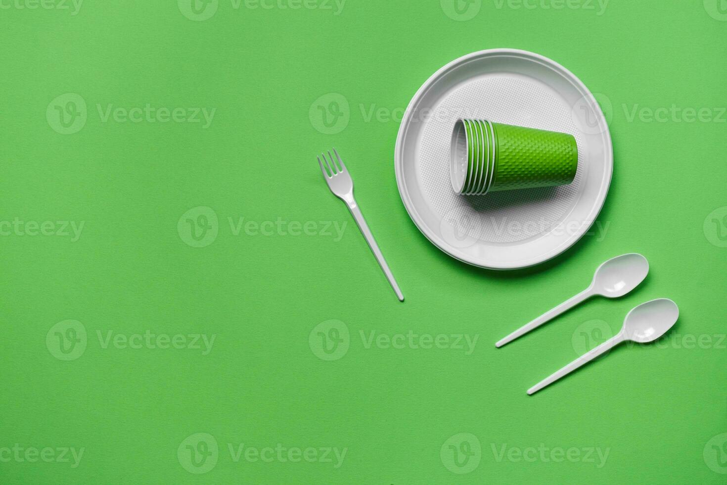Colorful plastic disposable tableware on green background with copy space. The concept of picnic utensil. Top view. Selective focus. Close-up. photo