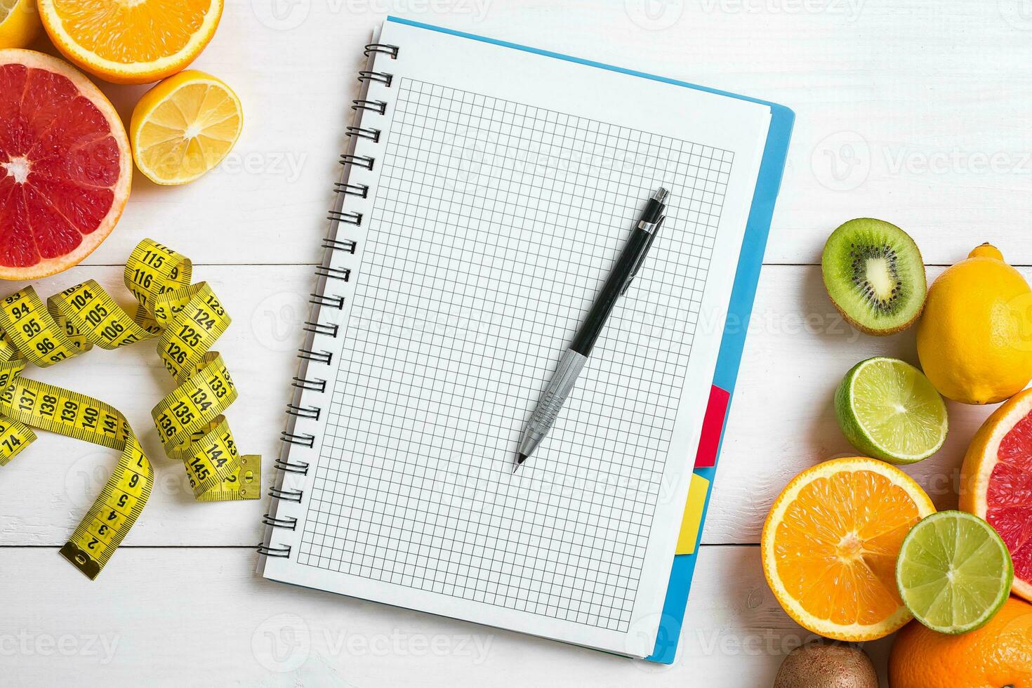 Fresh juice in glass from citrus fruits - lemon, grapefruit, orange, notebook with pencil on white wooden background photo